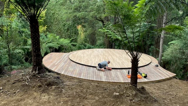 8 metre wooden circular yurt platform in a forest with a person working on it.