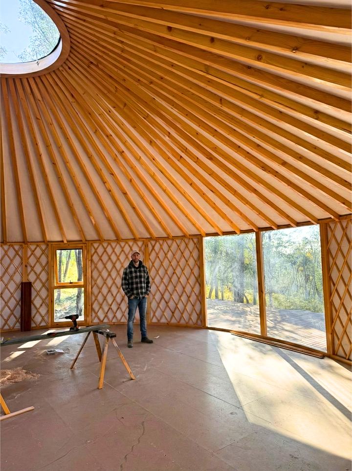 Person standing inside a 10 metre yurt with wooden interior and large windows.