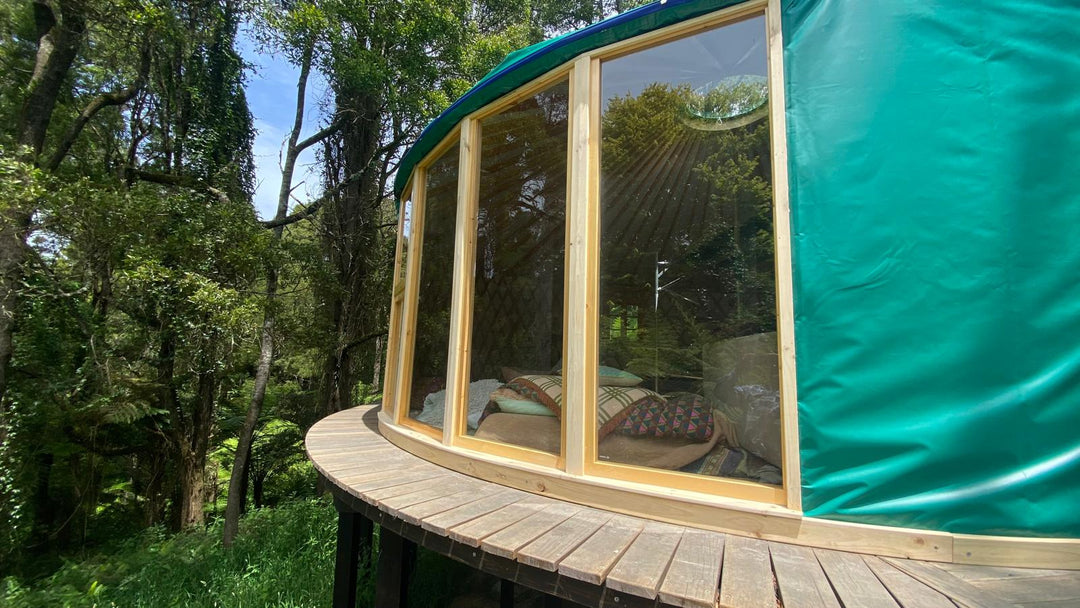 Round wooden yurt with large windows surrounded by trees
