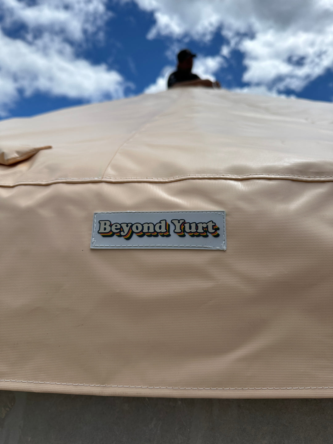 Beige yurt roof with 'Beyond Yurt' logo against a blue sky
