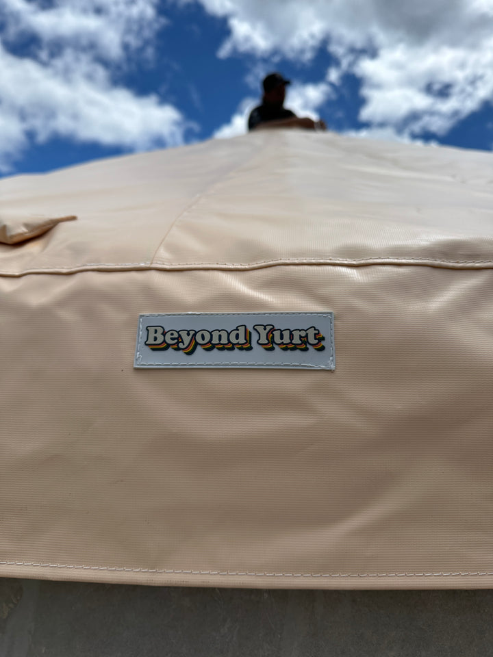 Beige yurt roof with 'Beyond Yurt' logo against a blue sky