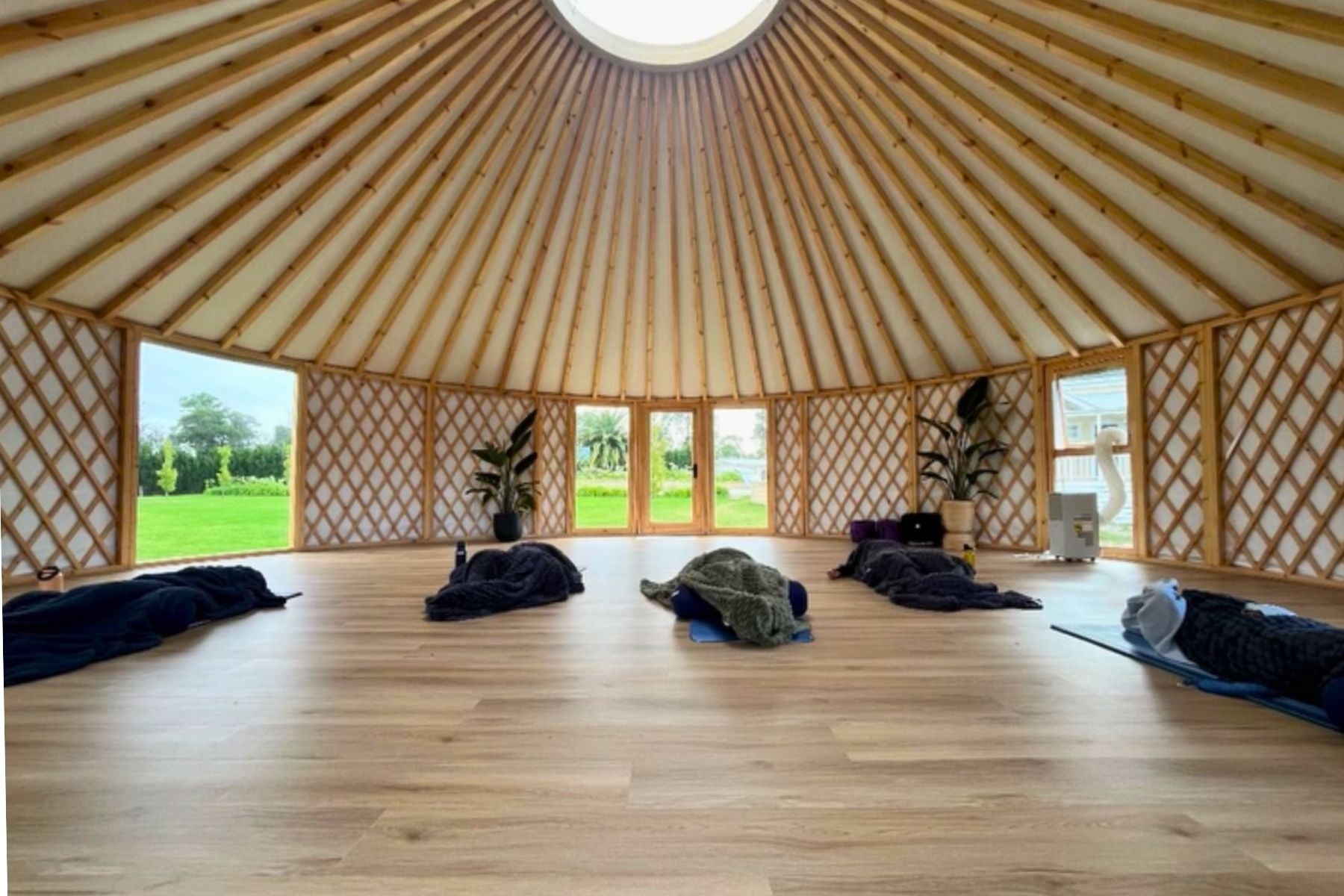 Modern yurt interior used as a wellness and retreat space with timber flooring, circular roof beams and large windows.