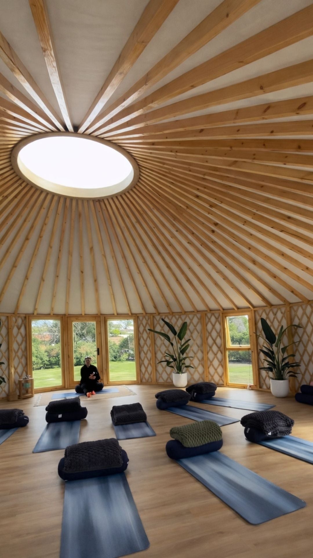 Modern yurt interior used as a wellness and retreat space with timber flooring, circular roof beams and large windows.