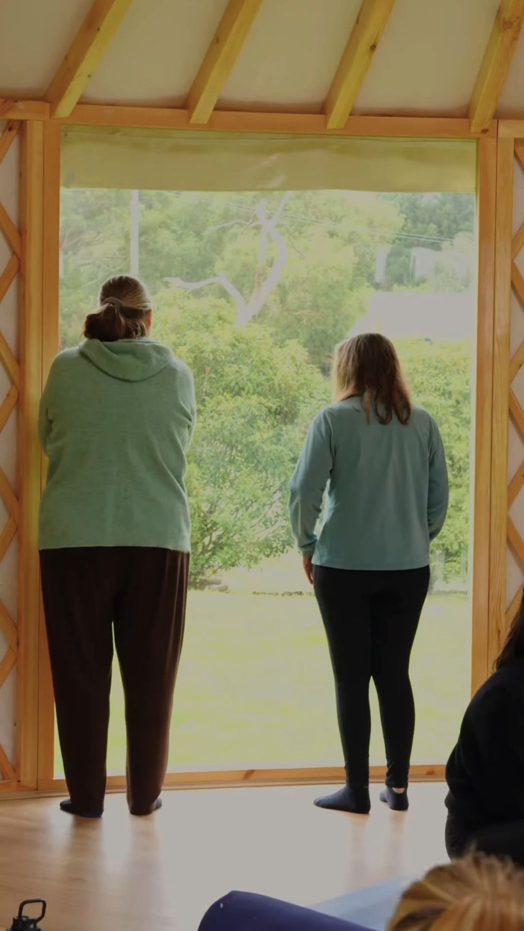 Two people standing inside a yurt looking out through large windows, showing a quiet private studio space connected to nature