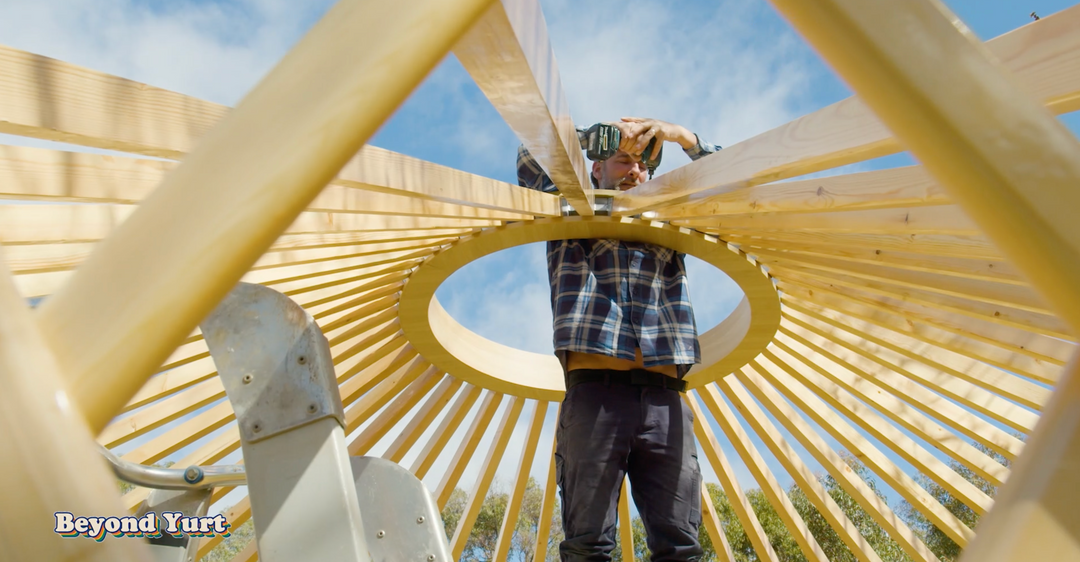 Person working on a wooden yurt structure with 'Beyond Yurt' branding.