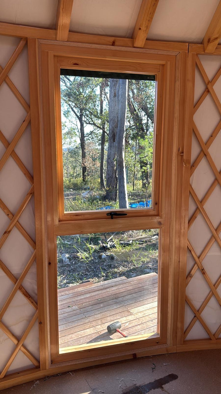 Wooden yurt window frame with glass window looking out at forest views